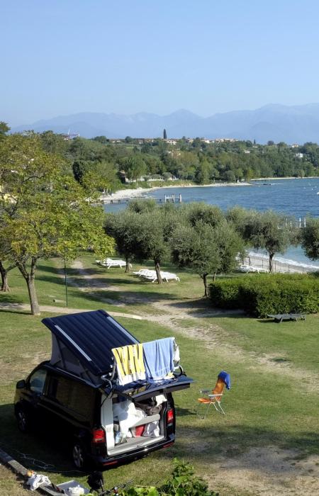 Camper in riva al lago con vista panoramica e montagne sullo sfondo.